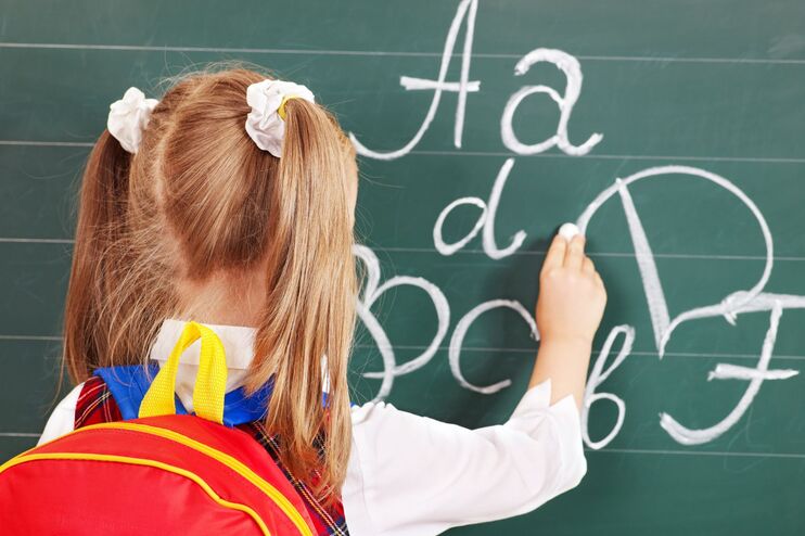 Ein Schulkind schreibt Buchstaben auf eine Tafel.