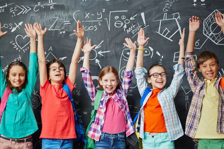Fünf Kinder stehen vor einer Tafel mit komplizierten Symbolen und recken die Arme in die Höhe.