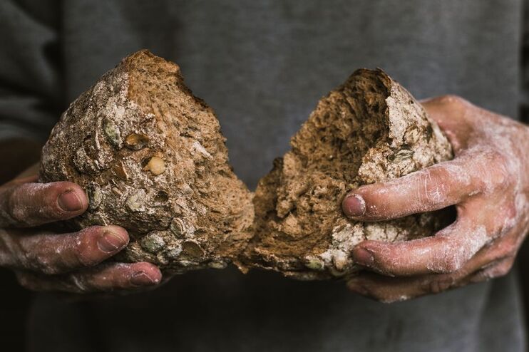 Zwei Hände, mit Mehl bestaubt, brechen ein dunkles Brot.