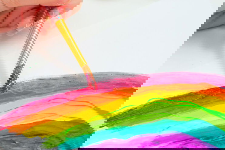 Eine Hand malt mit Tusche einen Regenbogen.
