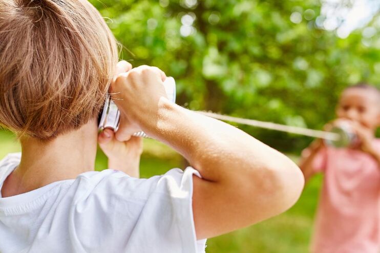 Zwei Kinder spielen mit einem Dosentelefon im Grünen.