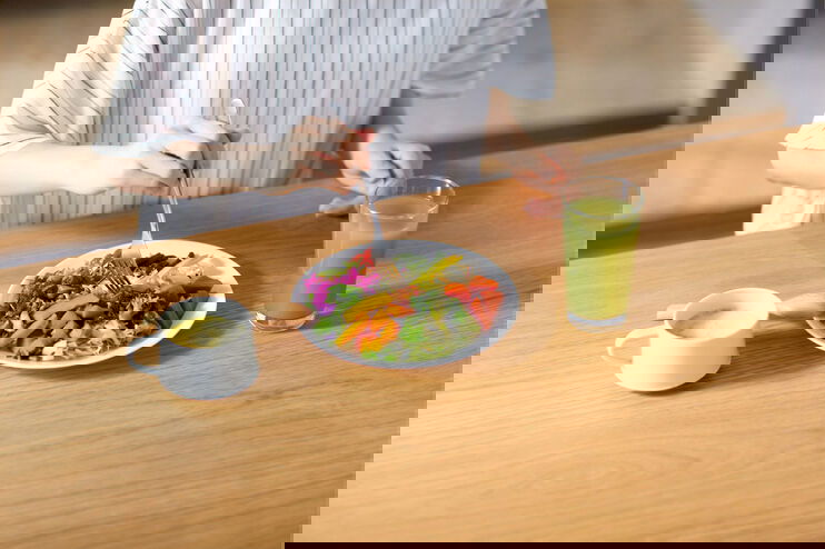 Eine Person sitzt an einem Tisch vor einem gesunden veganen Essen, einem Gemüse-Smoothie und einem Kaffee.