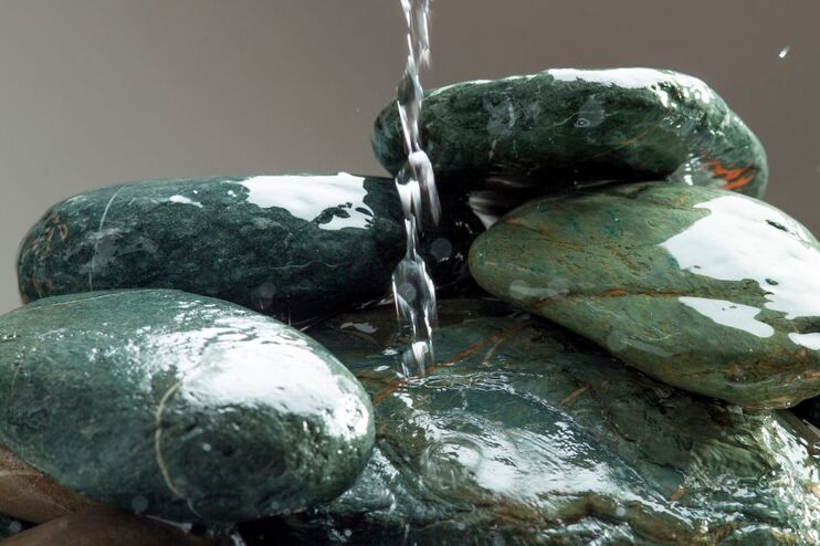 Ein Wasserstrahl läuft auf einen Haufen Steine hinunter.