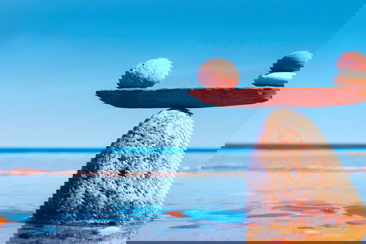 Ein großer Stein in flachem Wasser mit einem Brett darauf, auf dem kleinere Steine in einer Waage balancieren. Daneben steht: Soviel du brauchst.