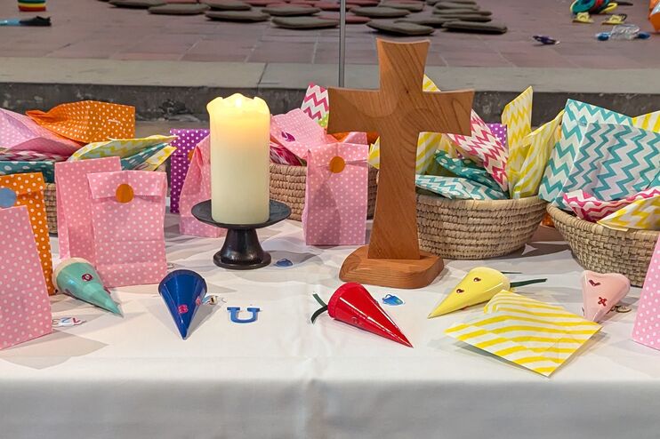 Auf einem Tisch stehen ein Kreuz aus Holz und mehrere bunte Papiertüten.