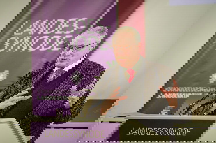 Eine männlich gelesene Person mit kurzen grauen Haaren am Redepult. 