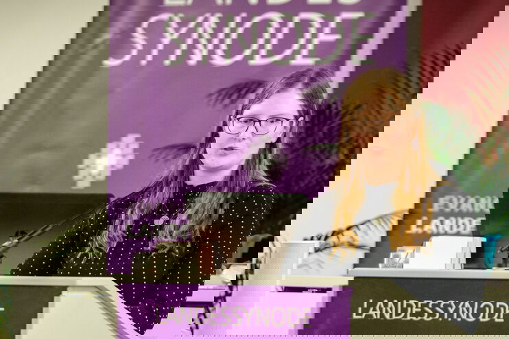 Eine weiblich lesbare Person steht am Podium und spricht.