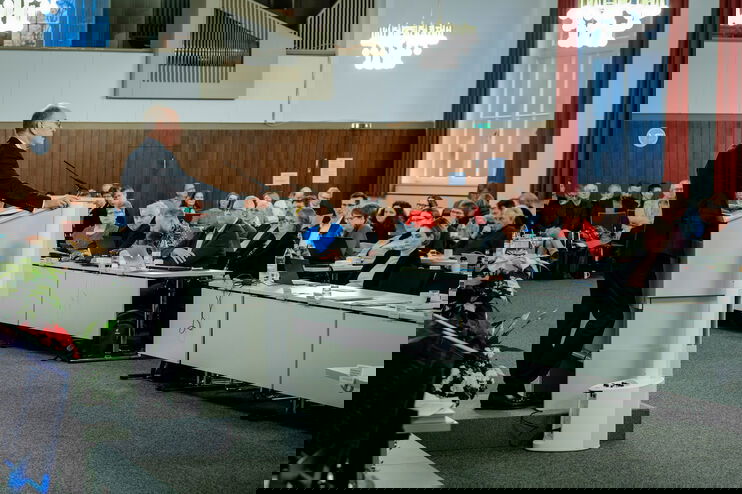 Eine männlich lesbare Person im Anzug steht am Podium