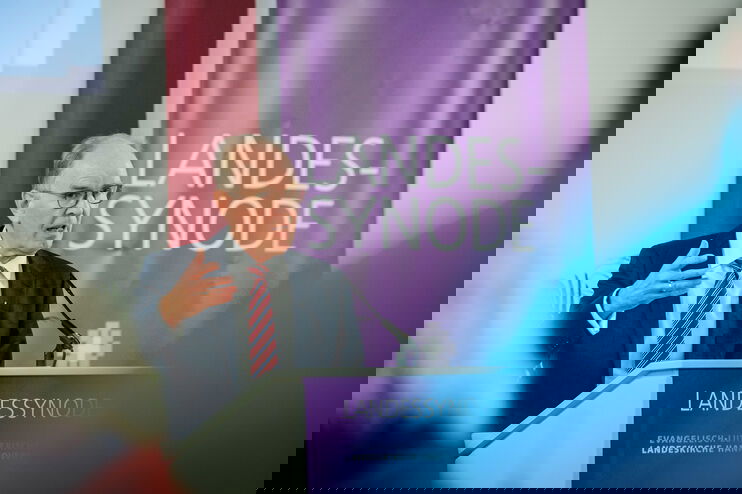 Eine männlich lesbare Person im Anzug steht am Podium