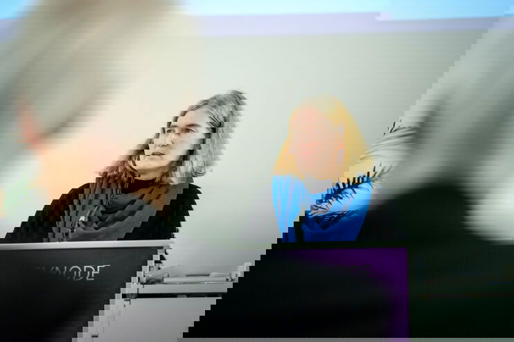 Eine weiblich lesbare Person steht am Podium und spricht.