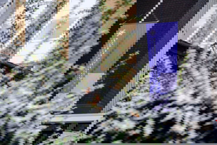 Das Bild zeigt eine schneebedeckte Hecke und im Hintergrund die Fahne der Landessynode.