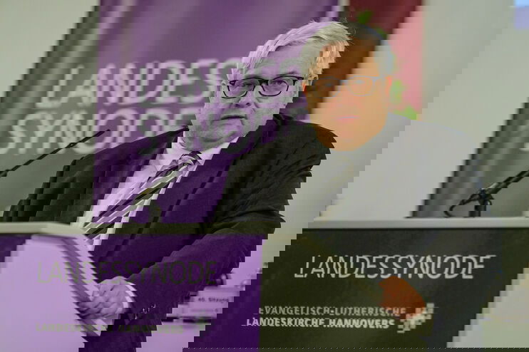 Eine männlich lesbare Person mit einer Brille steht an einem Rednerpult und spricht.