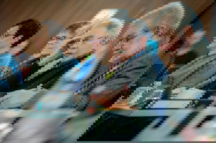 Eine Gruppe von Personen sitzt an einem langen Tisch und hört jemandem zu.