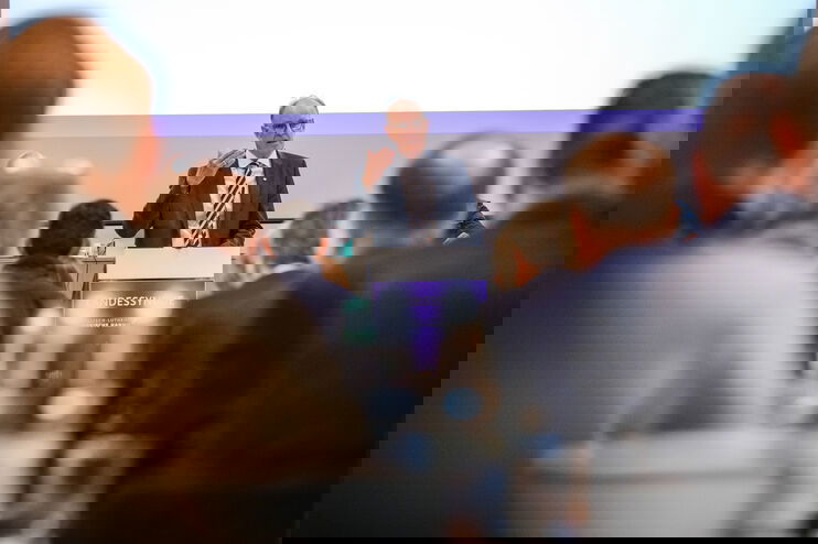 Eine Person redet und wurde durch Reihen von anderen Personen fotografiert