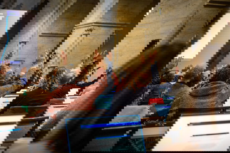 Mehrere Personen sitzen im Plenum und heben die Hand zur Abstimmung.