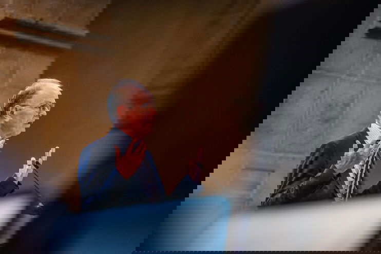 Eine männlich gelesene Person steht am Rednerpult und hebt beim Sprechen beide Hände. 