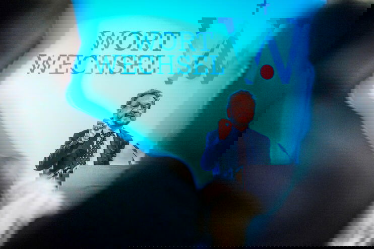 Ein Mann im Anzug spricht an einem Redepult, im Hintergrund auf der Leinwand steht „Wortwechsel“.