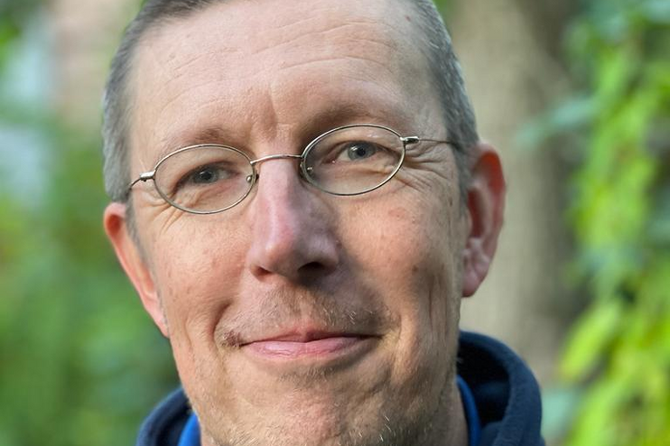 Ein mittelalter Mann mit kurzen Haaren und Brille lächelt in die Kamera.