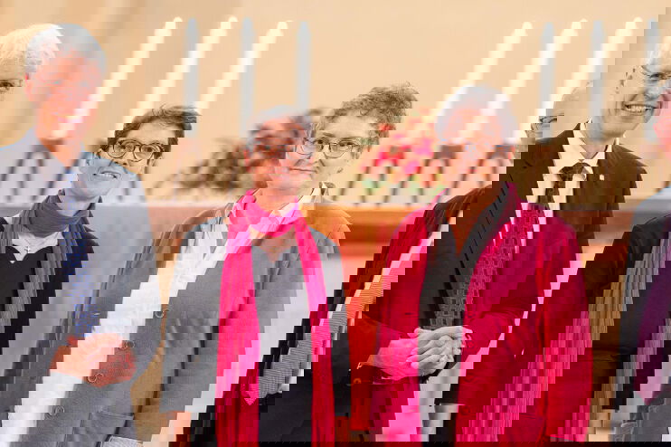 Vier Menschen stehen vor einem Kirchenaltar. Sie sind festlich gekleidet.