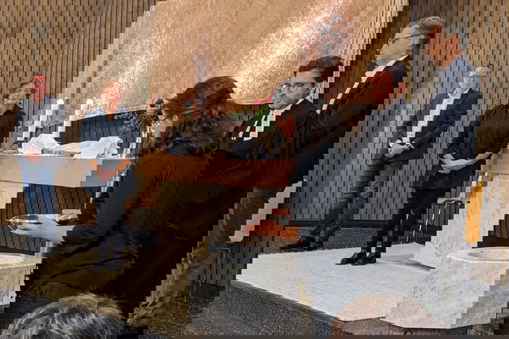 Eine Frau nimmt eine Taufschale aus einem Taufstein, vier weitere Personen stehen dabei.