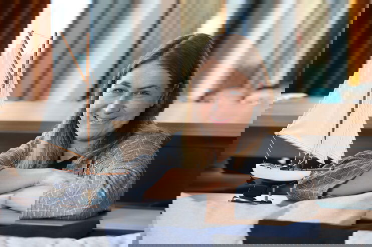 Eine Frau hat die Arme neben dem Modell eines Segelschiffs aufgestützt. 