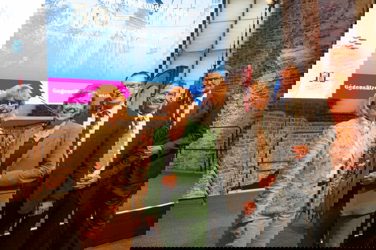 Zwei Frauen und drei Männer stehen vor einer Bühne mit einem Transparent im Hintergrund.