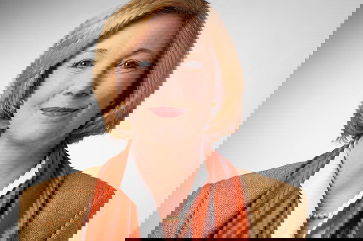 Eine Frau mit blonden Haaren, rotem Halstuch und Perlenkette.