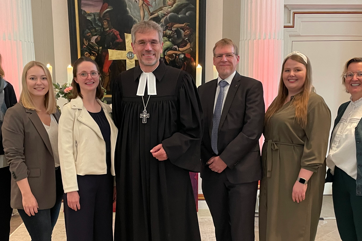 Mehrere Menschen stehen zusammen vor einem Altar. Einer trägt einen Talar.