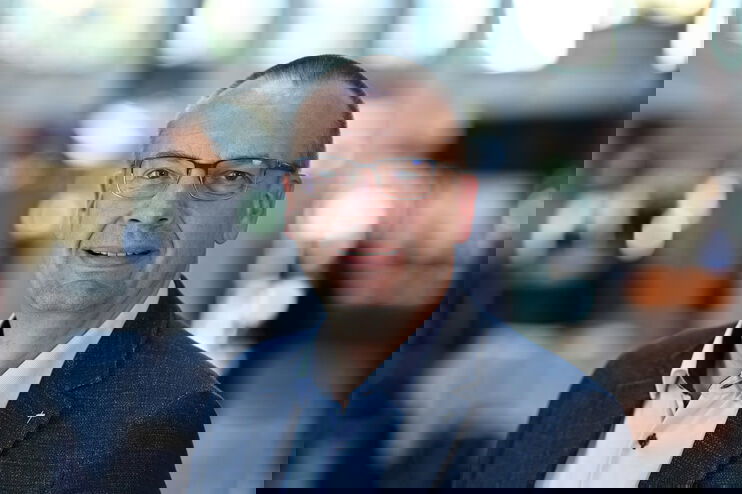 Eine als Mann lesbare Person im hellblauen Hemd und mit Sakko lächelt in die Kamera.