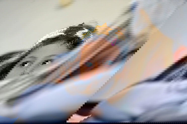 Ein Kind mit goldenen Sternen auf einem Stirnband blickt über die Schulter nach hinten. Es sitzt in einer Kirchenbank und ist nur mit halbem Gesicht zu erkennen.