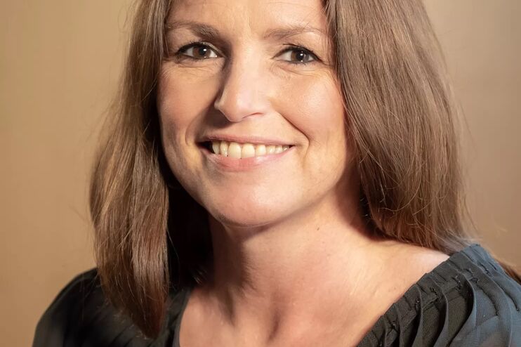 Eine Frau mit langen braunen Haaren und braunem Oberteil lächelt in die Kamera