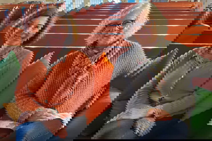 zwei Frauen sitzen auf Bänken mit bunten Sitzkissen in einer Kirche