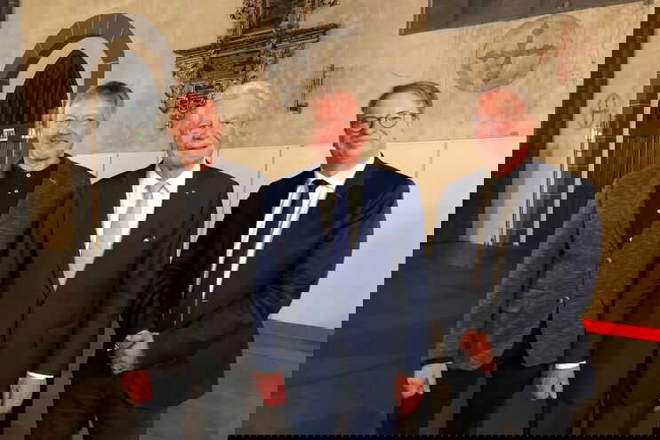 Drei Männer in Anzügen schauen in die Kamera.