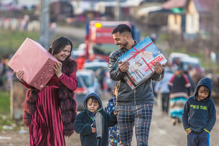 Zwei Erwachsene und zwei Kinder laufen, jeder ein Paket halten, eine Straße entlang.