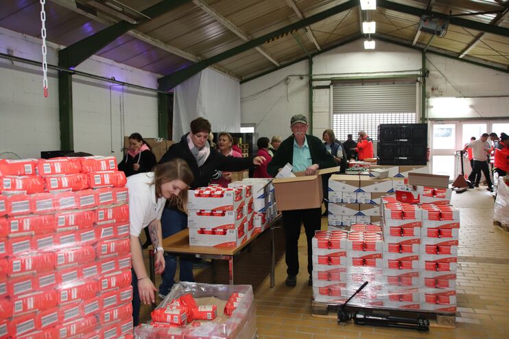 In einer Lagerhalle stehen Paletten voll Mehl und Zucker, einige Personen packen daraus kleinere Pakete an langen Tischen.