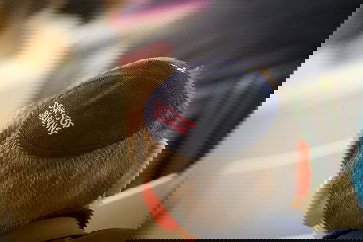 Vermutlich ein junger Mann sitzt in einer Stuhlreihe und trägt eine Kippah. Auf dieser steht in rot-rosa: Don't stop believing.