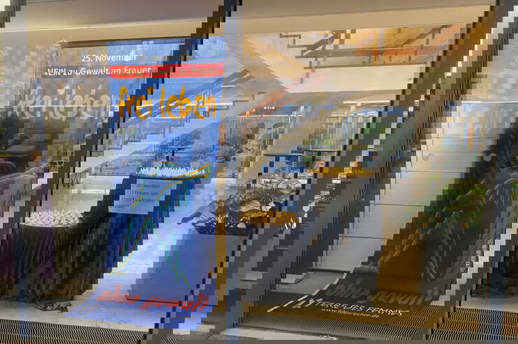 Ein Aufsteller und Teelichter weisen hinter einer großen Glasscheibe auf den Tag gegen Gewalt an Frauen hin.