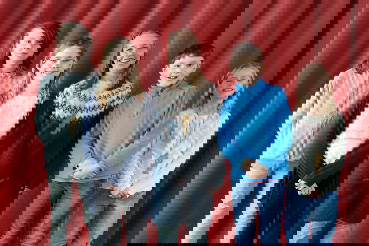 Fünf Kinder stehen vor einem roten Vorhang und lächeln in die Kamera.