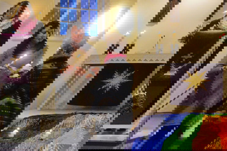 drei Frauen stehen bei einem Kirchenaltar und entzünden eine Kerze.