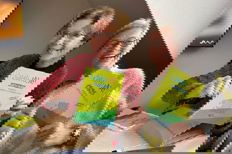 Zwei Frauen zeigen ein grünes Liederbuch mit dem Titel Lalelu-JA!