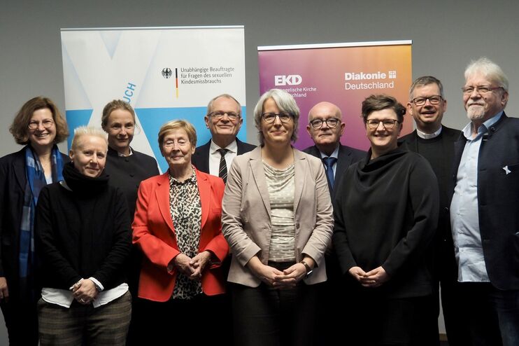 Mehrere Frauen und Männer haben sich vor Aufstellern der Bundesregierung, der EKD und der Diakonie zum Gruppenbild aufgestellt.