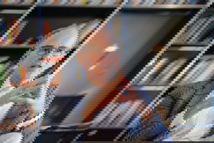 Ein mittelalter Mann mit hoher Stirn sitzt vor einer Bücherwand