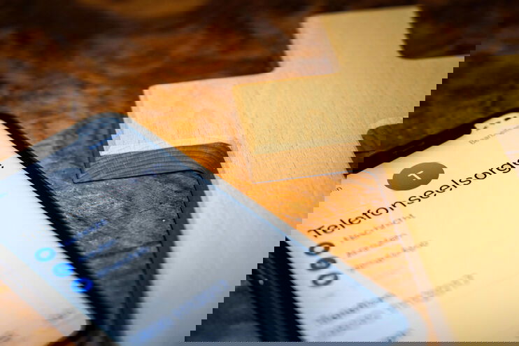 Neben einem Kreuz liegt ein Mobiltelefon, auf dem Telefonseelsorge zu lesen ist.