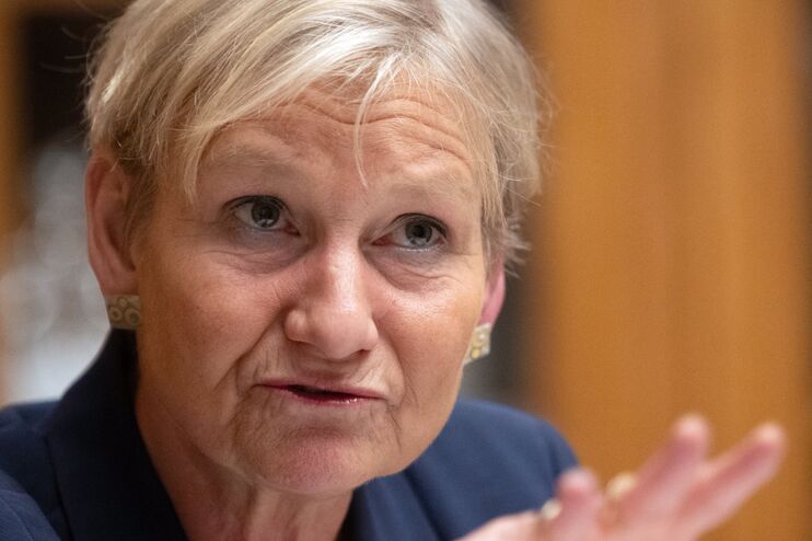 eine Frau spricht und gestikuliert. Sie sitze vor einem Bücherregal. Die Frau hat kurze, blonde Haare.