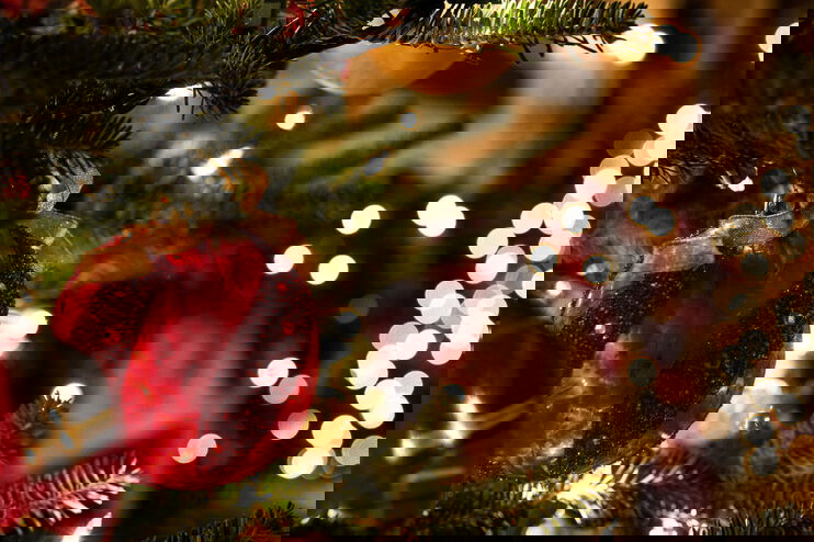 rote Christbaumkugeln an einem Weihnachtsbaum. Im Hintergrund sieht amn Lichterkerzen.