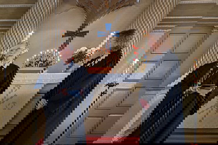 Zwei Frauen in Talaren stehen vor einem Altar mit Kanzel darüber.