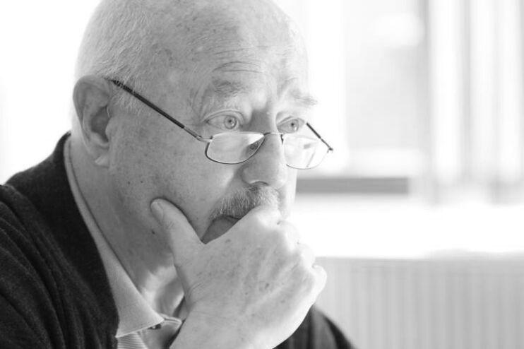 Ein schwarzweißes Bild von einem Mann mit schmaler Brille. Er stützt sich nachdenklich auf eine Hand. 