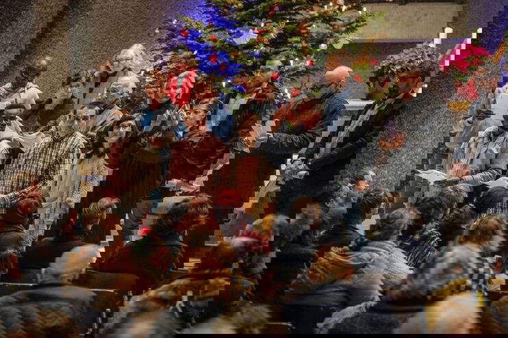 Mehrere Menschen, offenbar unterschiedlicher Herkunft, stehen nebeneinander auf den Stufen vor einem Altarraum. Vor ihnen sitzen dutzende Menschen.