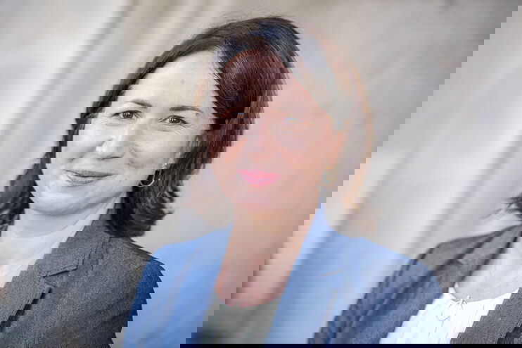 Eine als Frau lesbare Person mit schulterlangen dunklen Haaren lächelt in die Kamera.