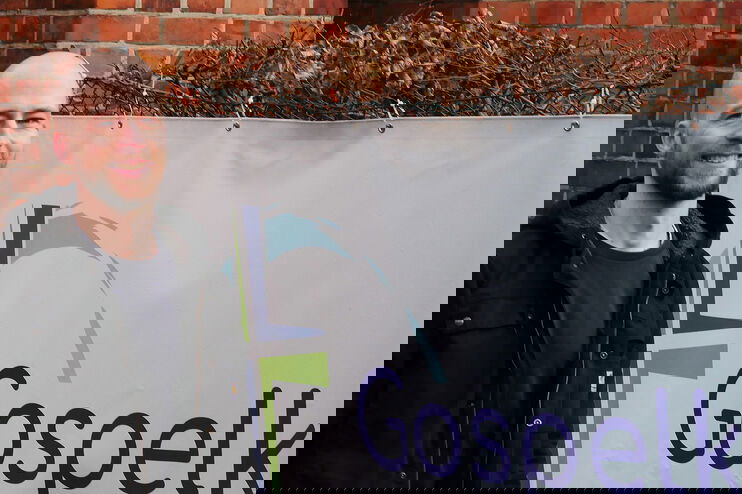 Ein Mann mit Glatze und Bart steht vor einem Transparent mit der Aufschrift Gospelkirche Hannover.